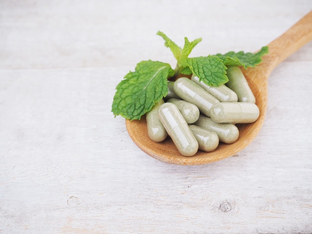 Pilules à base de plantes et feuilles de menthe sur cuillère en bois