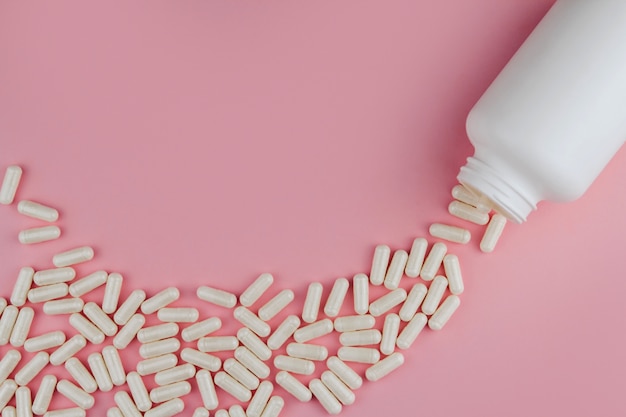 Pilules blanches sur un espace de copie de mur rose. Comprimés épars. Bouteille en plastique avec des pilules.