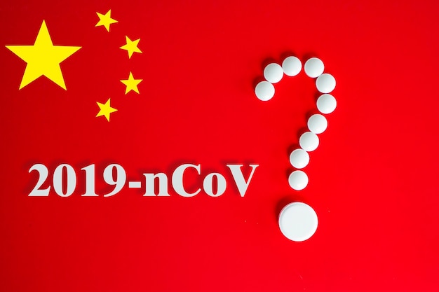 Pilules blanches sous forme de point d'interrogation sur fond rouge avec inscription 2019-nCoV et espace de copie pour le texte. Fond rouge du drapeau chinois. 2019 Concept du nouveau coronavirus 2019-nCoV.
