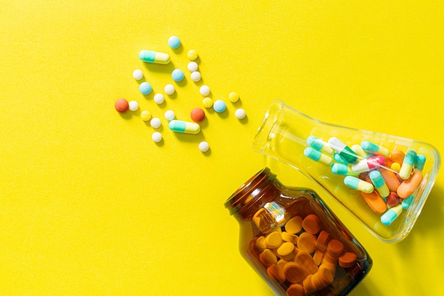 Pilules et bouteilles de pilules sur fond jauneComprimés et capsules de pilules multicolores de bouteille en verre