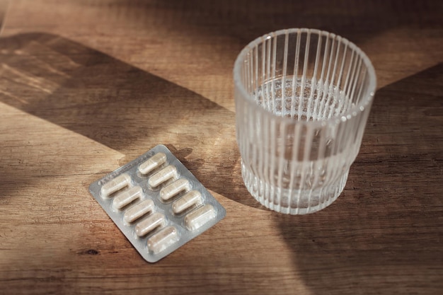 Pilules capsules médecine et verre d'eau sur fond de bois