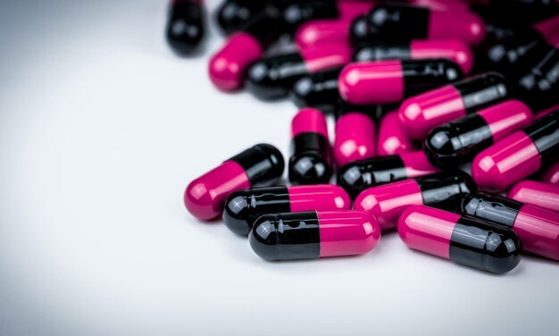 Photo pilules en capsules noires et roses sur table blanche résistance aux antibiotiques soins de santé mondiaux pills en capsules antimicrobiennes arrière-plan de la pharmacie utilisation raisonnable d'antibiotiques dans l'industrie pharmaceutique