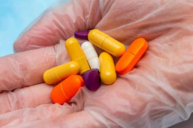 Pilules colorées, comprimés à la main dans un gant médical. Protection des médicaments, traitement des virus, antiviraux, concept de maladies.