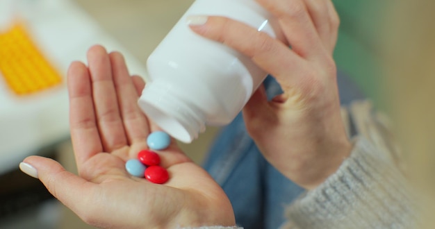 Des pilules colorées tombent sur une paume de femme à partir d'une bouteille de pilules. Fermer. Concept de pharmacie et de traitement, vue rapprochée.