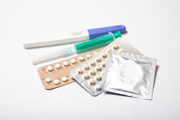 Pilules contraceptives et préservatifs sur fond blanc