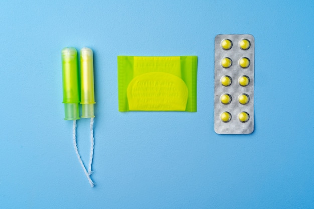 Pilules contraceptives, serviettes hygiéniques et tampons sur fond bleu