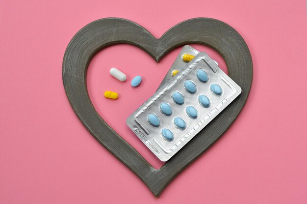 Pilules dans un cadre en forme de coeur sur fond rose