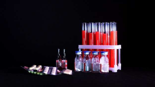 Pilules sur fond de tubes à essai avec liquide rouge et ampoules sur fond noir.