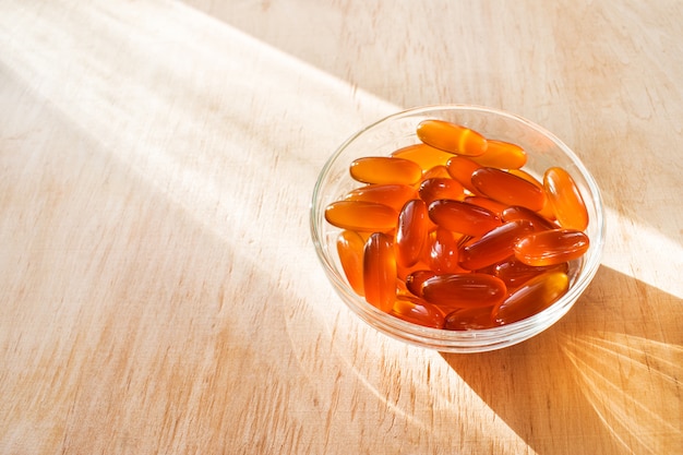 Pilules de gel de lécithine dans un bol en verre rond avec lumière du soleil sur fond en bois