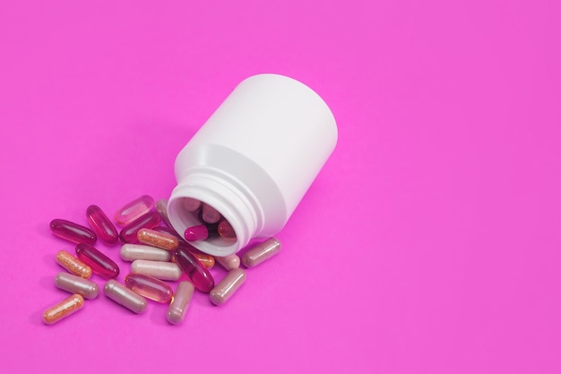 Pilules et gélules multicolores sur fond rose