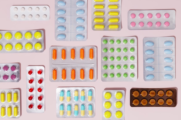 Pilules et gélules pharmaceutiques colorées emballées sous blisters sur fond rose