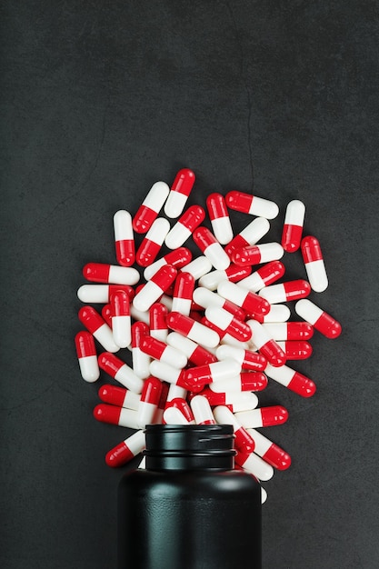 Pilules rouges et blanches d'un pot noir sur fond noir.