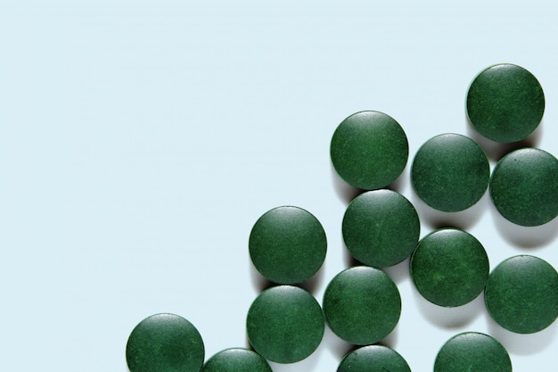 Pilules de spiruline, comprimés verts sur une surface bleue