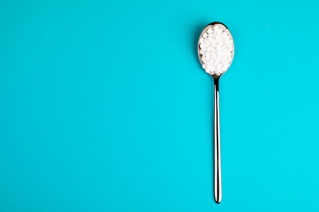 Photo pilules de substitut de sucre dans une cuillère, sur fond bleu.