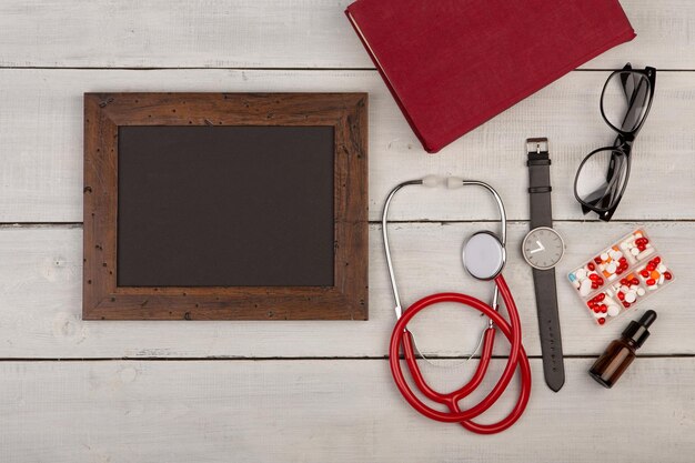 Pilules de tableau noir blanc livre stéthoscope lunettes et montre sur fond de bois