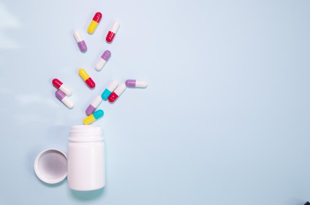 Les pilules de vitamines sont posées à plat sur un fond bleu dans une bouteille en plastique blanche. Prescription médicale de vitamines.