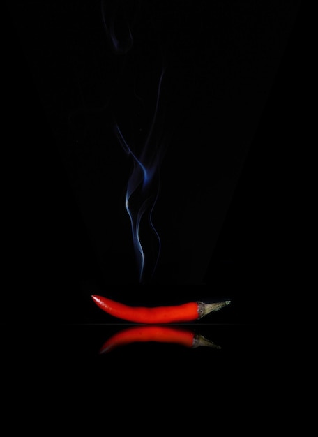 Le piment rouge avec de la fumée se trouve sur un fond sombre de surface brillante noire