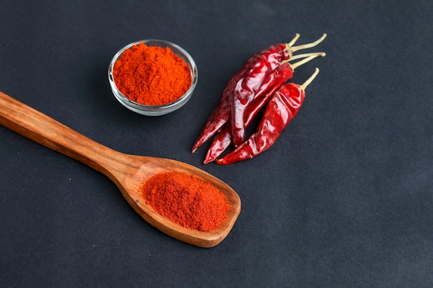 Piment rouge séché et poudre dans un bol en verre et cuillère en bois sur une surface sombre