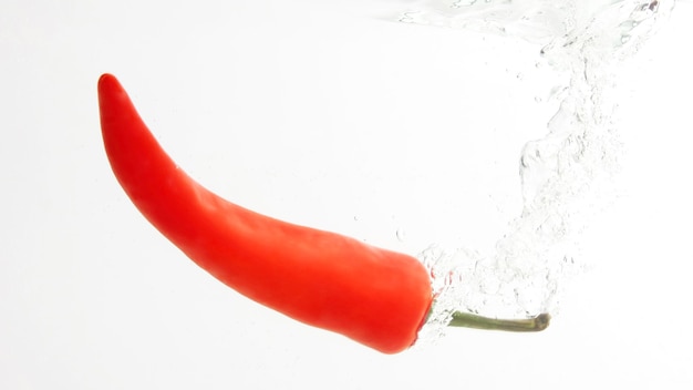 Piment rouge tombant dans l'eau. légumes et aliments frais et sains