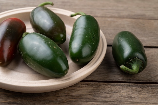 Piments jalapenos verts sur une assiette sur une table en bois.