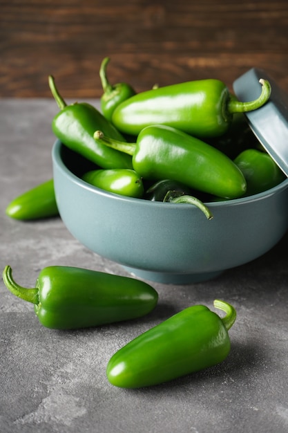 Piments jalapenos verts dans un bol en céramique sur fond gris, gros plan, vertical.