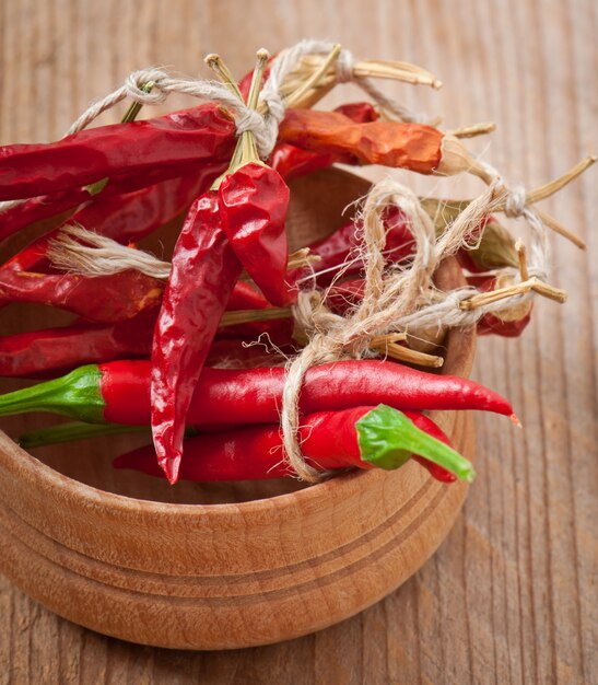 Piments rouges chauds attachés avec une corde sur un bol en bois