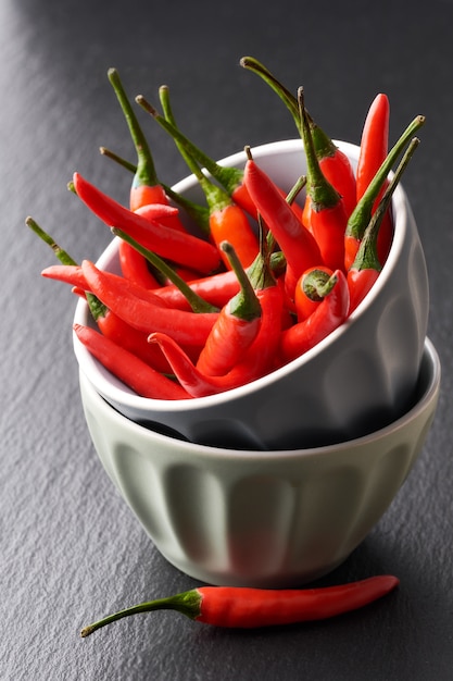 Piments rouges dans une pile de deux bols en céramique grise sur pierre ardoise noire