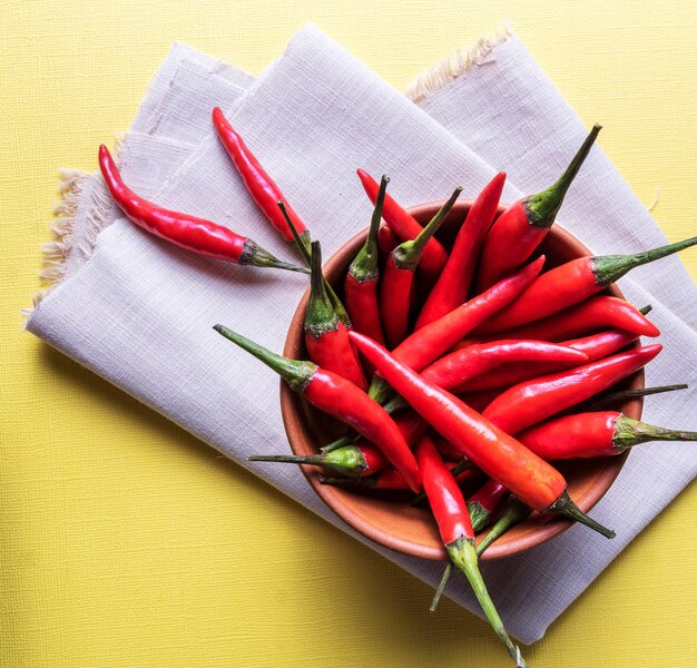 Piments rouges mûrs dans un bol sur une surface jaune