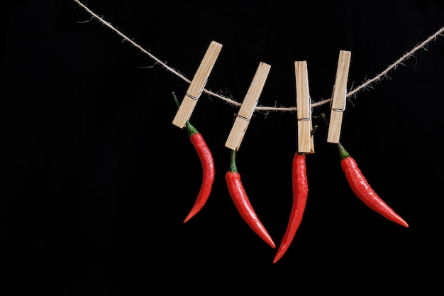 Piments rouges pendent sur une pince à linge sur une corde sur un fond noir. Épice chaude. Fermer.