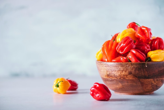 Piments Scotch Bonnet colorés dans un bol en bois sur fond gris Copier l'espace