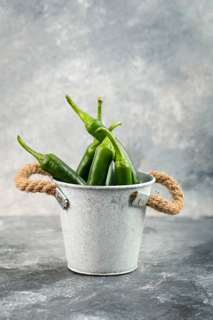 Piments verts dans un seau placé sur une table en marbre.