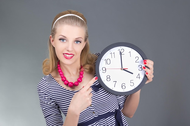 Pin-up en robe rayée tenant l'horloge sur gris