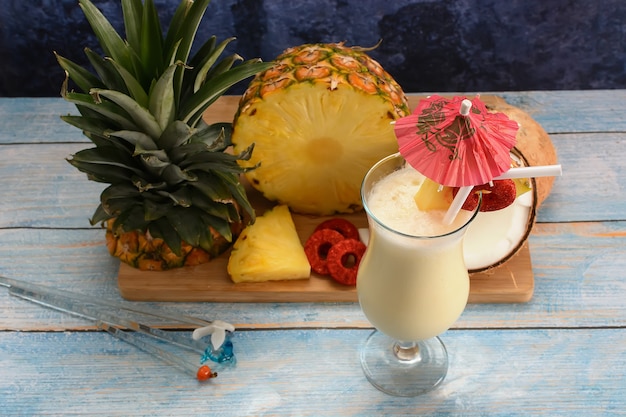 Piña colada avec des fruits frais sur une planche à découper en bois sur une table de tableau blanc et fond bleu