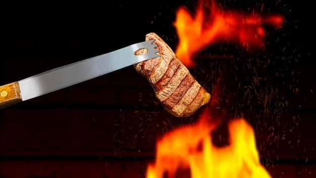 Pince à barbecue tenant un steak sur le gril avec le feu