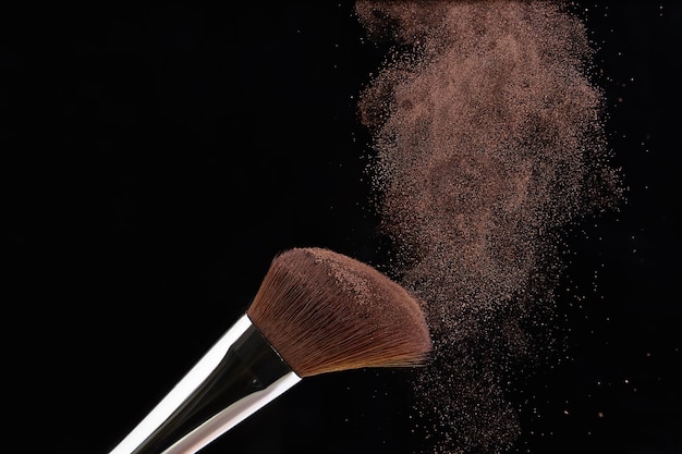 Photo pinceau de maquillage avec des éclaboussures de poudre pour le visage sur fond noir