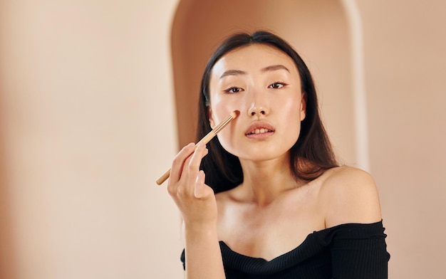 Pinceau de maquillage Jeune femme asiatique sérieuse debout à l'intérieur