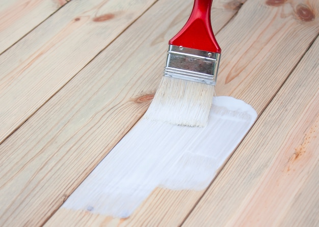 Le pinceau peint des planches de bois avec de la peinture blanche