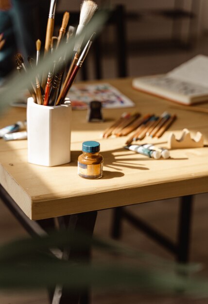 Pinceau avec tubes de peinture à l'huile et crayons de couleur. Outils d'art et d'artisanat, encre, table en bois. Peinture pour artistes contemporains. Objets pour la créativité des adultes. Dessin à l'aquarelle. Photo moderne atmosphérique