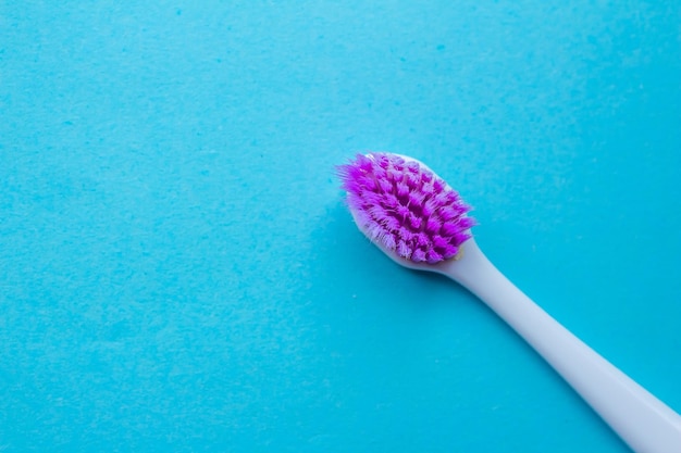 Un pinceau violet et blanc avec un manche violet repose sur une surface bleue.