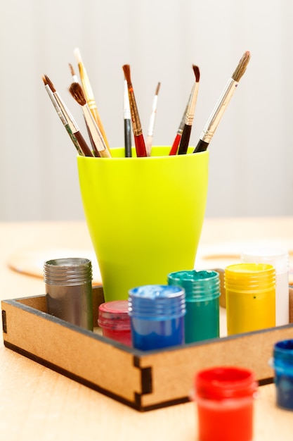 Pinceaux dans une tasse et peintures en boîte sur table en bois