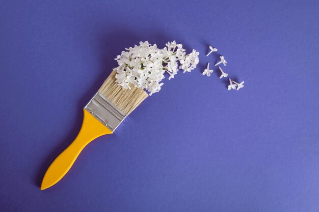 Pinceaux jaunes en bois et fleurs blanches de lilas sur fond violet foncé