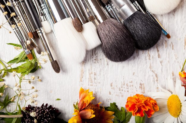 Pinceaux de maquillage cosmétiques à côté de fleurs sauvages sur fond de bois