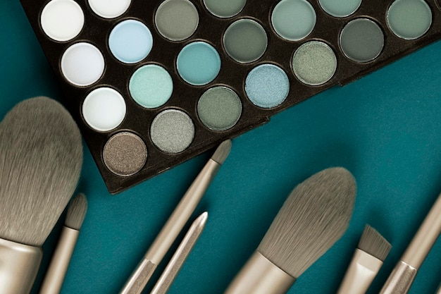 Pinceaux de maquillage professionnels de couleur dorée avec palette d'ombres à paupières sur fond bleu Concept créatif à la mode Close up Flat lay