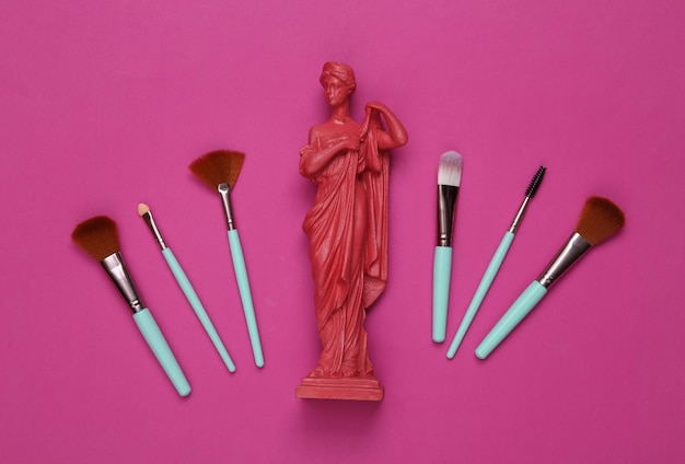 Pinceaux de maquillage et statue antique sur fond rose Scène glamour de beauté Vue de dessus