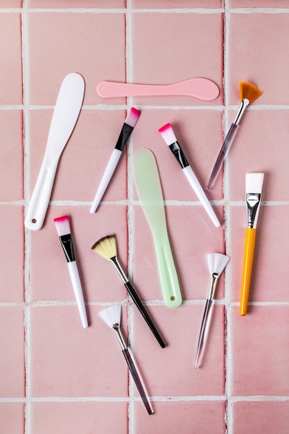 Photo pinceaux et spatules pour appliquer un masque facial sur fond carrelé rose