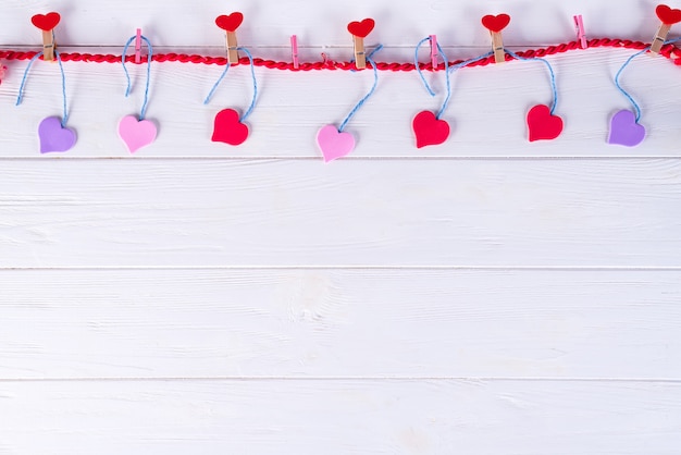 Pinces à linge avec des coeurs rouges sur un ruban sur un fond en bois blanc. Saint Valentin