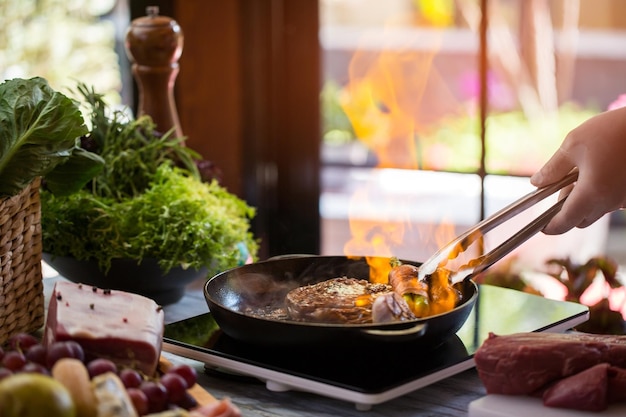 Pinces touchant la viande sur la poêle. Nourriture frite. Comment faire un steak flambé. Plat cher dans un nouveau restaurant.