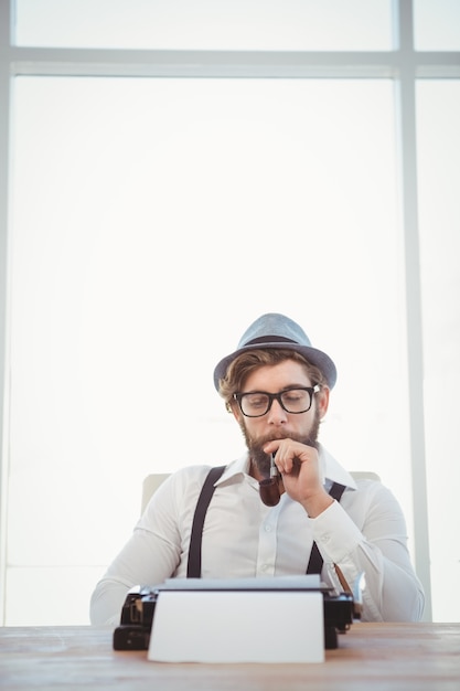 Pipe fumer hipster tout en étant assis en regardant la machine à écrire