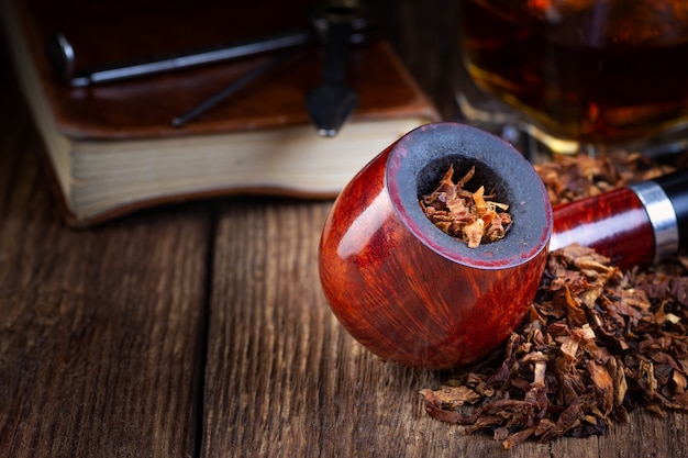 Pipe à fumer laquée, tas de tabac et boisson alcoolisée sur une table en bois vintage.