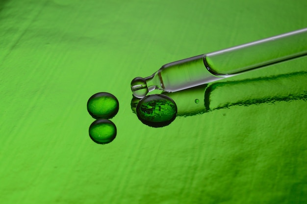 une pipette cosmétique avec du liquide se trouve sur un fond vert recouvert de gouttes. fermer.
